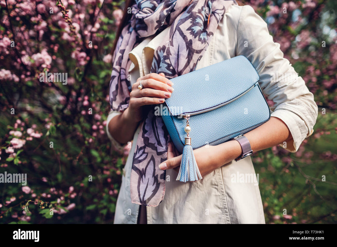 Giovane donna azienda blu Elegante borsetta e indossare abiti alla moda in giardino. Molla femmina di capi di abbigliamento e accessori. La moda Foto Stock