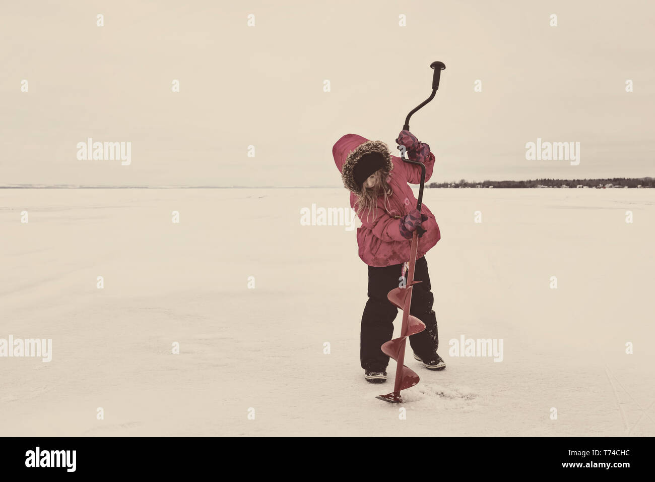 Ragazza giovane cercando di praticare un foro nel ghiaccio del Lago Ghiacciato Wabamun senza alcun successo: Wabamun, Alberta, Canada Foto Stock
