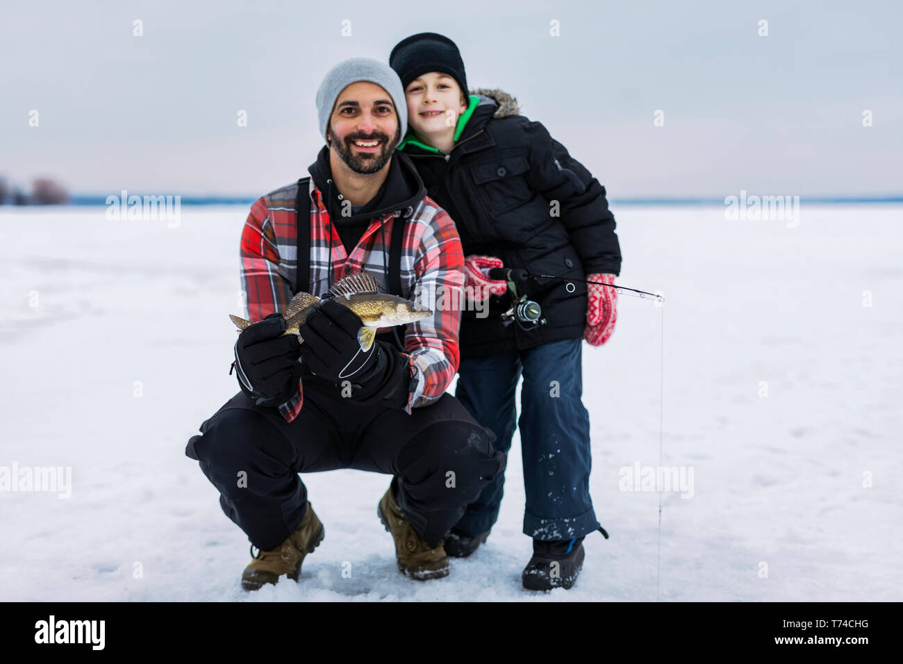 Padre e figlio giovane in mostra le loro catture di walleye prima di rilasciarlo mentre la pesca sul ghiaccio al lago Wabamun; Wabamun, Alberta, Canada Foto Stock