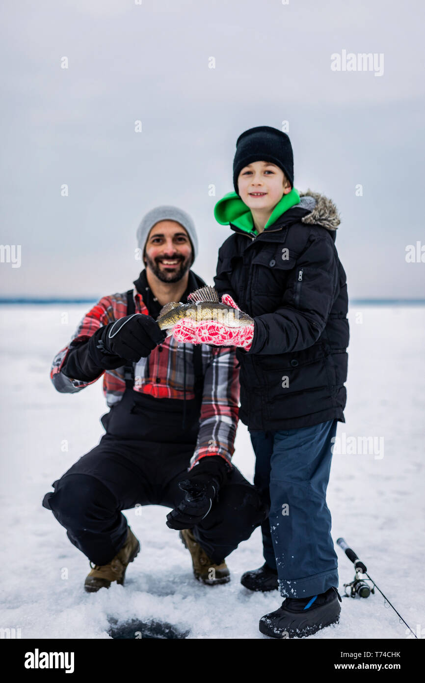 Padre e figlio giovane in mostra le loro catture di walleye prima di rilasciarlo mentre la pesca sul ghiaccio al lago Wabamun; Wabamun, Alberta, Canada Foto Stock