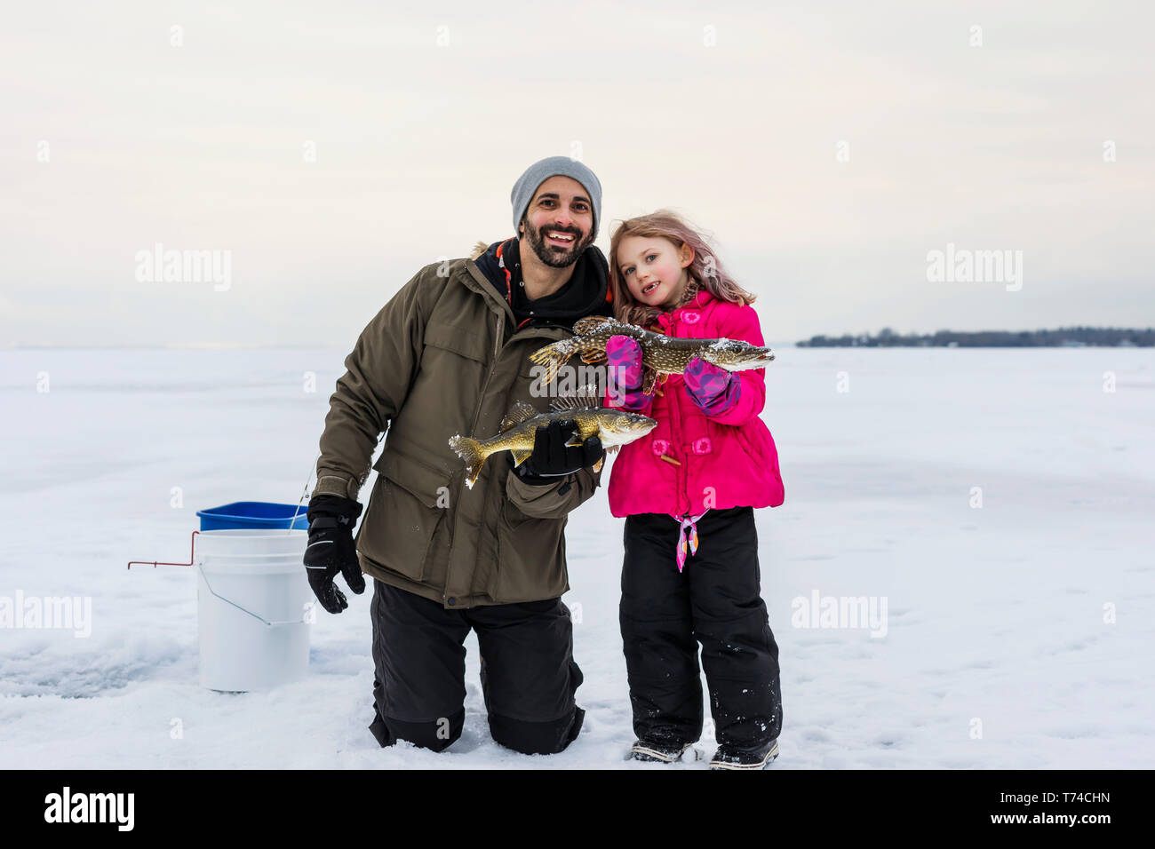 Padre e figlia giovane in mostra le loro catture prima di rilasciarlo mentre la pesca sul ghiaccio al lago Wabamun; Wabamun, Alberta, Canada Foto Stock