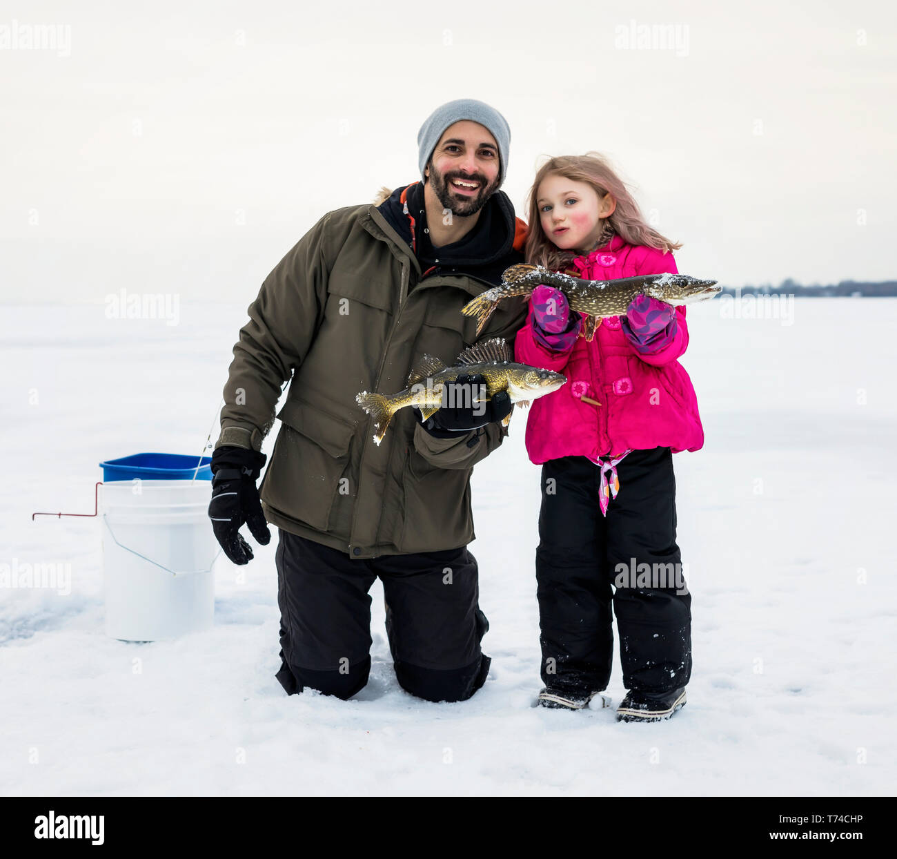 Padre e figlia giovane in mostra le loro catture prima di rilasciarlo mentre la pesca sul ghiaccio al lago Wabamun; Wabamun, Alberta, Canada Foto Stock