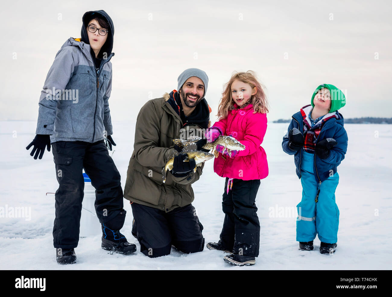 Padre e quattro figli in mostra le loro catture prima di rilasciarlo mentre la pesca sul ghiaccio al lago Wabamun; Wabamun, Alberta, Canada Foto Stock