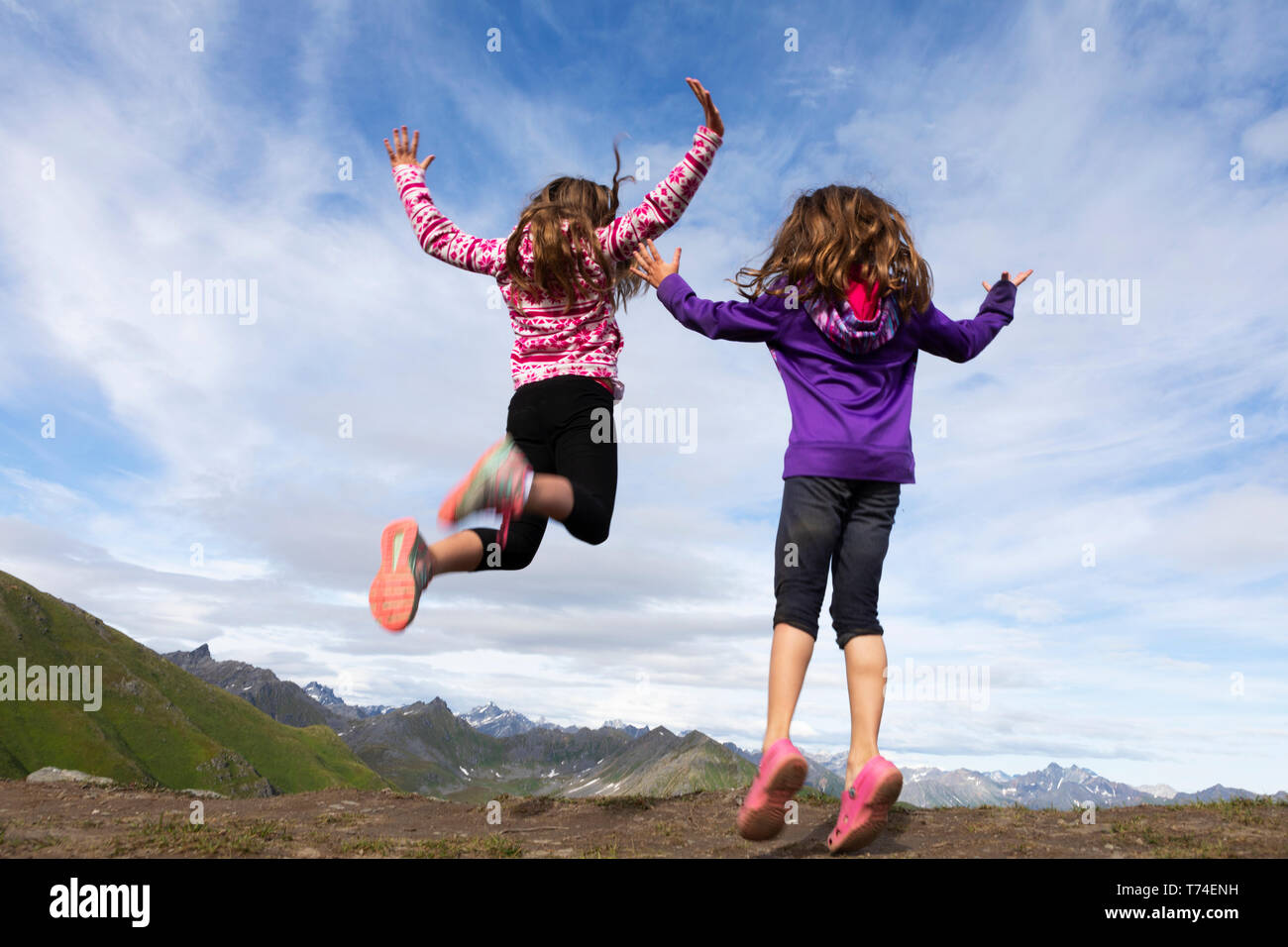 Due giovani sorelle saltando in Talkeetna montagne, Hatcher's Pass; Alaska, Stati Uniti d'America Foto Stock