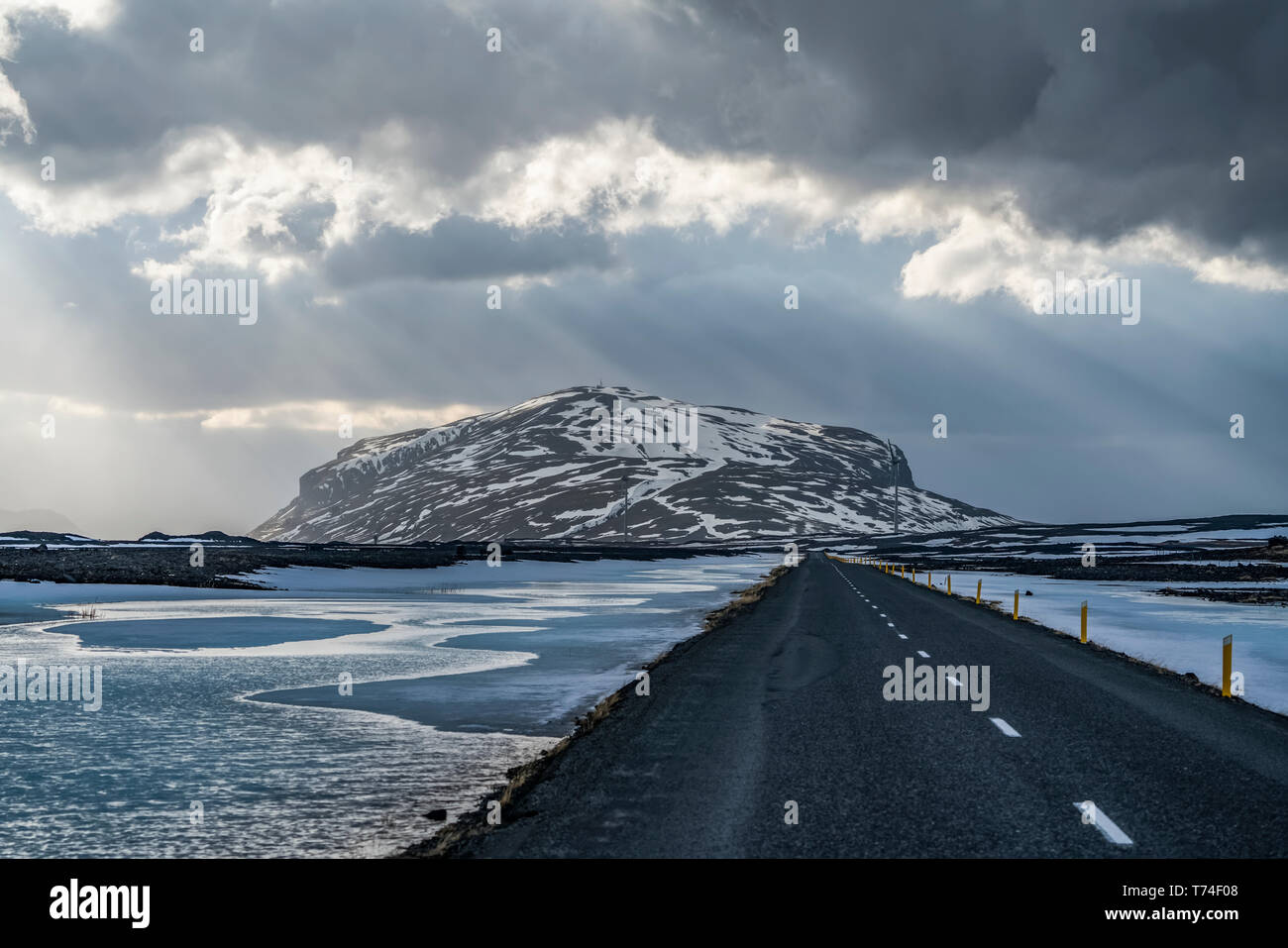 Strada che conduce nel drammatico paesaggio di Islanda mentre il sole splende attraverso le nuvole facendo una bella scena; Islanda Foto Stock