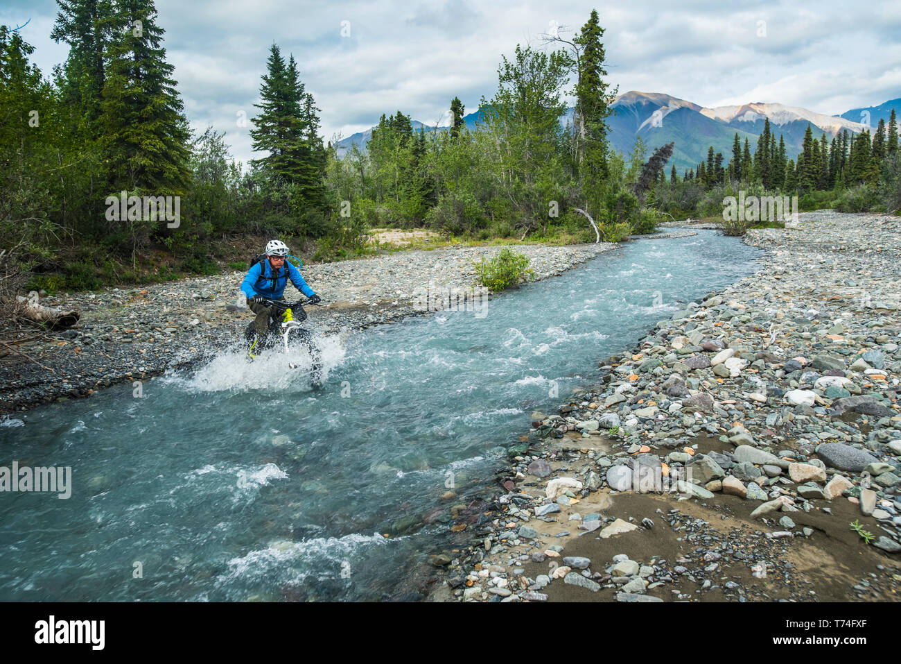 Un uomo grasso biking attraverso un flusso di Wrangell-St. Elias National Park e conservare in un nebbioso giorno di estate nel centro-sud della Alaska Foto Stock
