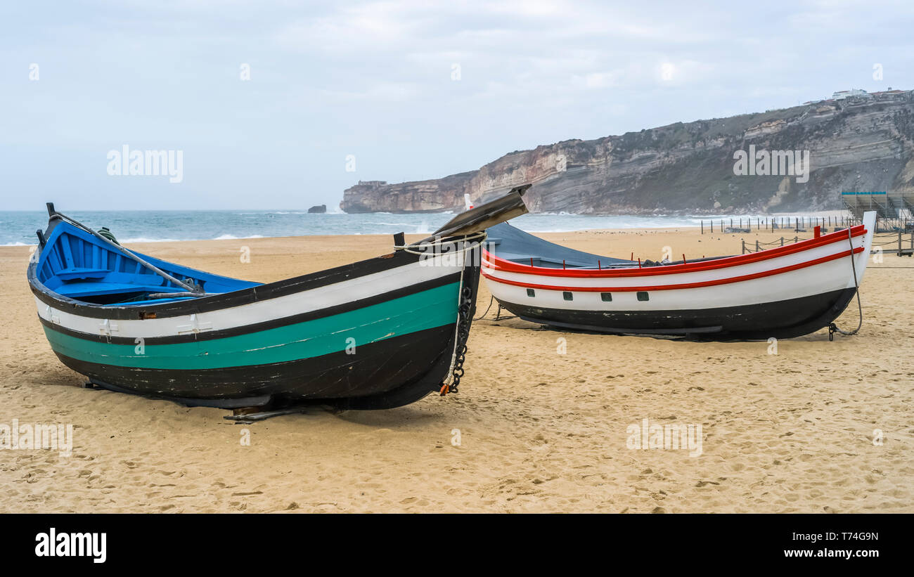 Due coloratissimi, imbarcazioni a remi in legno sulla spiaggia della località balneare di Nazare; Nazare, Distretto di Leiria, Portogallo Foto Stock