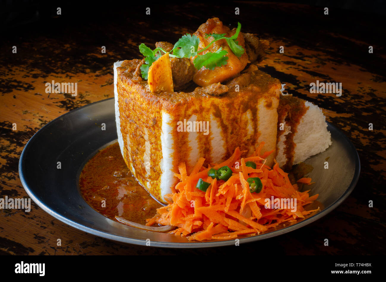 Un coniglietto di Durban Chow - o, in questo caso un quarto di montone bunny - servita con sambals. Questo è un iconico Durban pasto composto da una sezione di una forma di pane Foto Stock