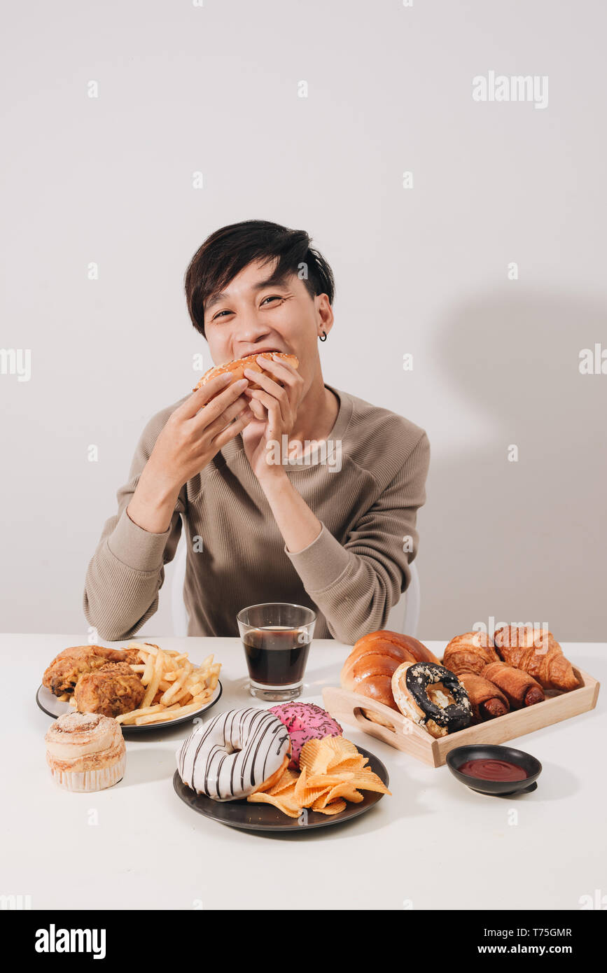 Ritratto di uomo asiatico seduto e snacking ciambelle isolate su sfondo bianco. Uomo grasso concetto di dieta Foto Stock