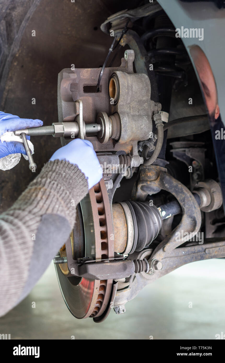 Mechanic cambiando le pastiglie dei freni di un veicolo e premere il pistone della pinza del freno Foto Stock