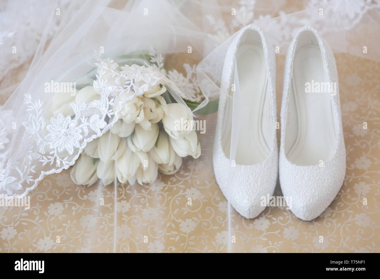 Wedding bouquet di tulipani bianco coperto con un velo accanto alla sposa bianco ad alta scarpe a tacco Foto Stock
