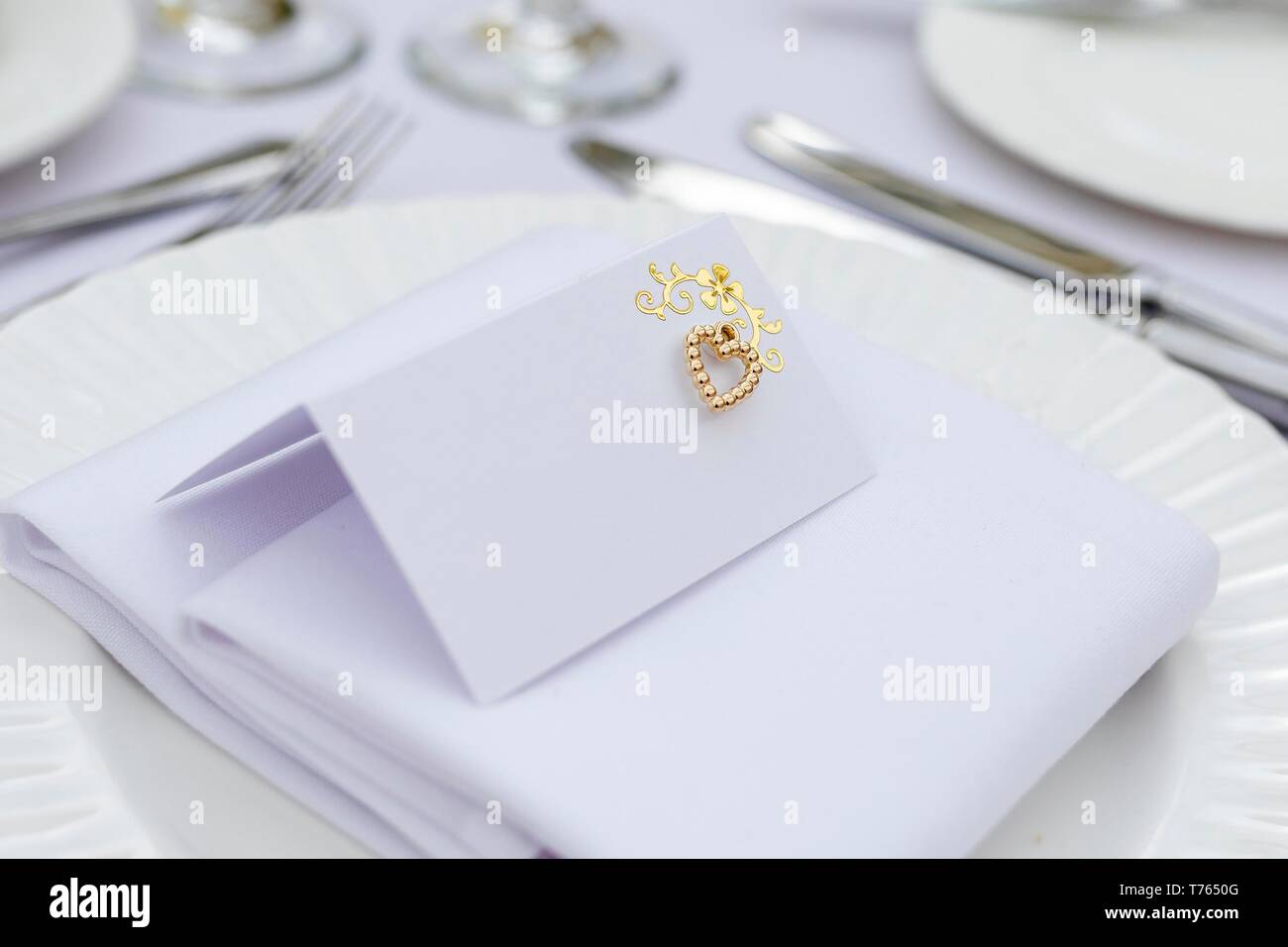 Close up di un vuoto bianco minimalista Luogo di matrimonio card con un ornato oro decorazione di cuore. Foto Stock