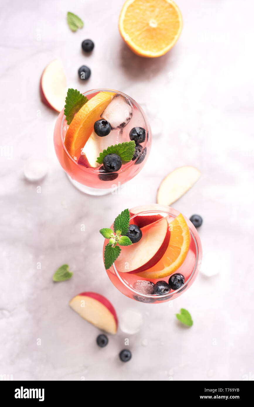 Vino di colore rosa Sangria bevanda con frutta e mirtilli su marmo bianco, copia dello spazio. Vetro a freddo estate iced pink sangria cocktail. Foto Stock