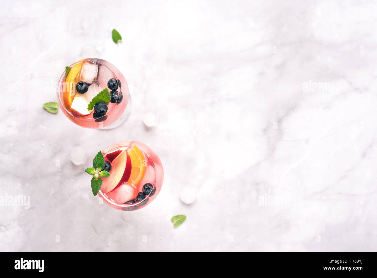 Vino di colore rosa Sangria bevanda con frutta e mirtilli su marmo bianco, copia dello spazio. Vetro a freddo estate iced pink sangria cocktail. Foto Stock