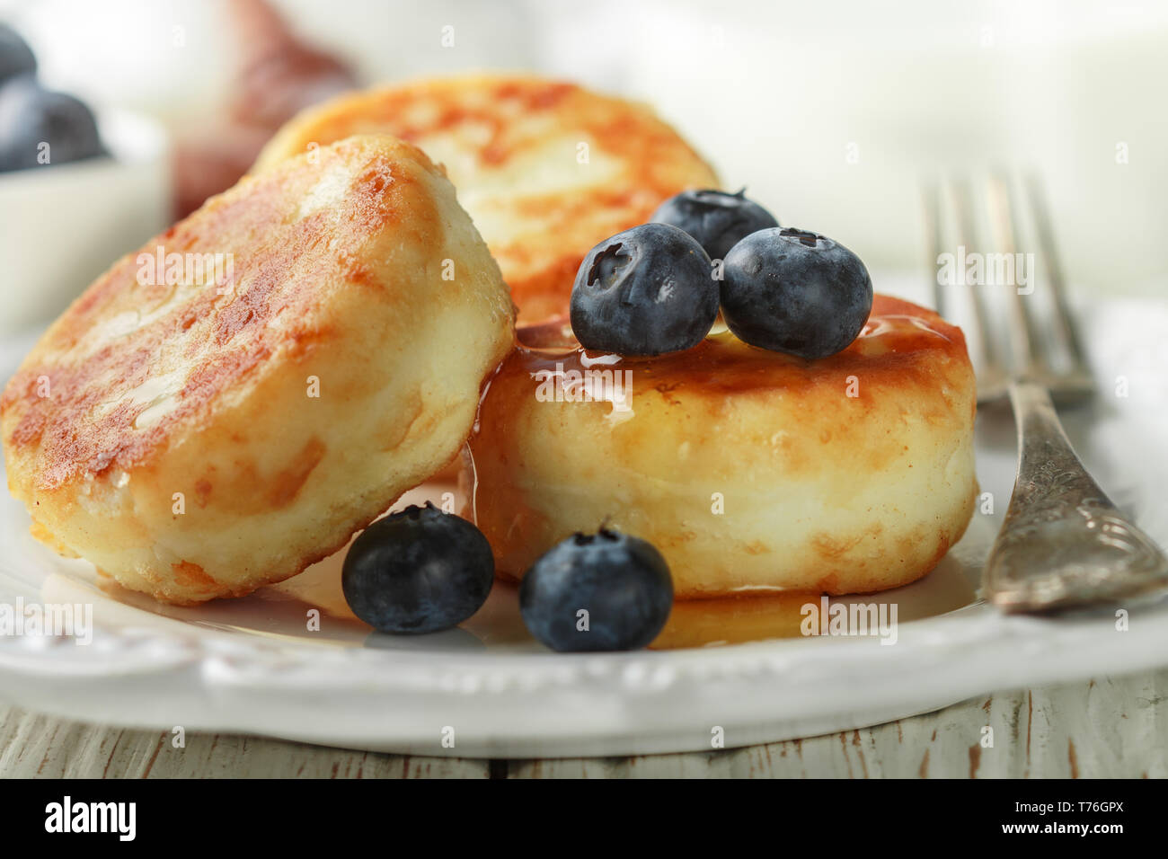 Cottage cheese pancakes, syrniki, frittelle di cagliata con frutti di bosco freschi mirtillo e miele in una piastra bianca. Colazione Gourmet. Messa a fuoco selettiva Foto Stock