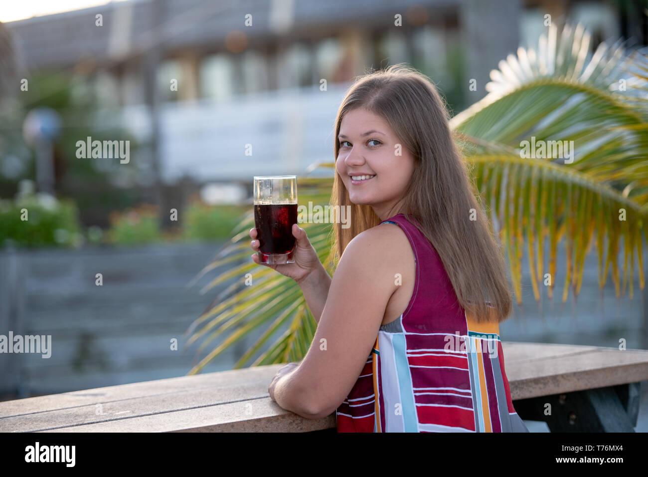 Giovane e bella donna che indossa abiti di bere succo di frutta sulla spiaggia al mattino sullo sfondo di palme in Florida Foto Stock Giovane e bella donna che indossa abiti di bere succo di frutta sulla spiaggia al mattino sullo sfondo di palme in Florida Foto Stock