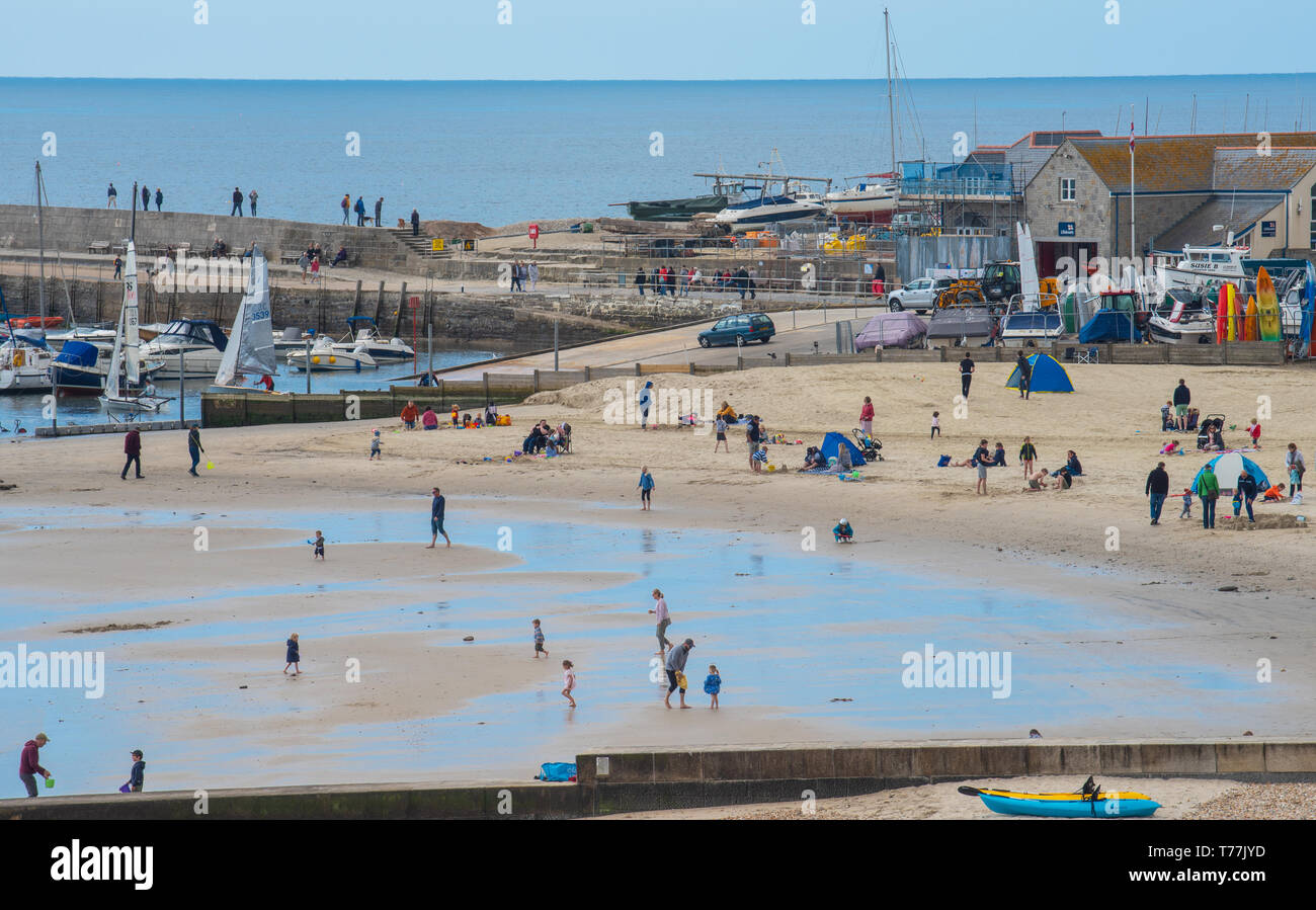 Lyme Regis, Dorset, Regno Unito. Il 5 maggio 2019. Regno Unito: Meteo visitatori godere di caldo e soleggiato incantesimi con una leggera brezza sulla spiaggia a Lyme Regis. Le condizioni dello scambiatore di calore sono previsti per il week-end festivo di maggio. Credito: Celia McMahon/Alamy Live News. Foto Stock