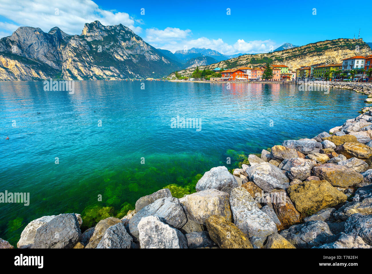 Lungomare roccioso e la città con i suoi edifici colorati, lago di Garda, Torbole, Italia, Europa Foto Stock