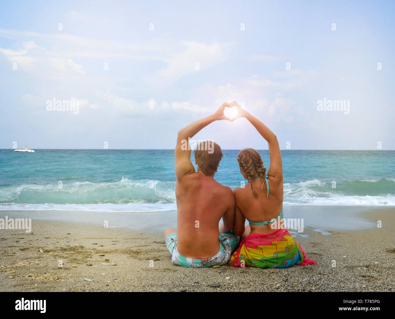 Coppia giovane in amore seduto sulla spiaggia e ripiegate le sue mani a forma di cuore, attraverso il sole risplende. Il concetto della luna di miele, amore Foto Stock