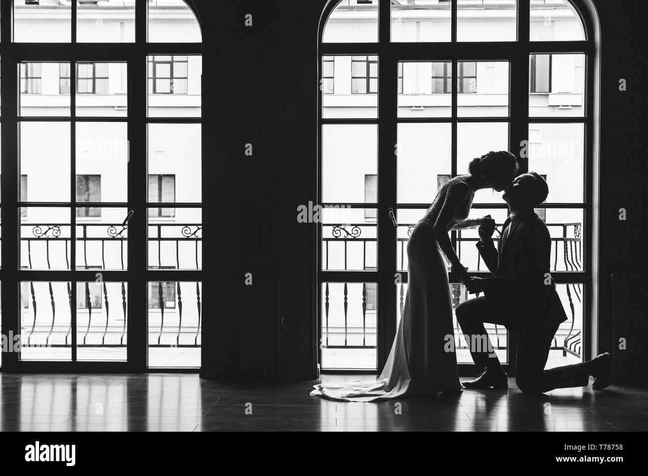 Sagome di un uomo in tuta e donne in un vestito e con un bouquet di fiori. L'uomo si è inginocchiato davanti al suo amante, ha preso la mano e la baciò Foto Stock