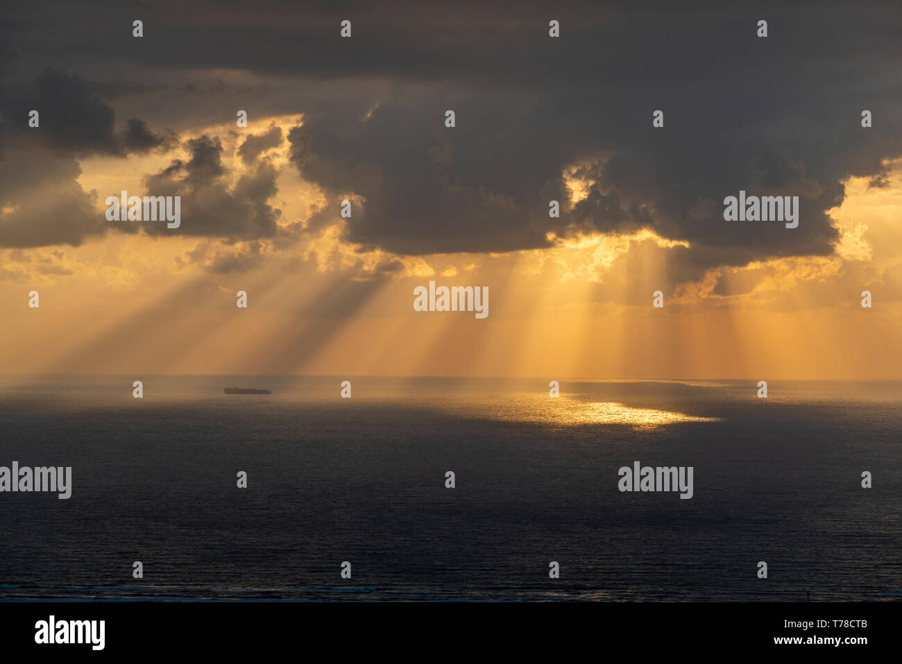 Raggi di sole colata attraverso le nuvole nel mare e una nave portacontainer Foto Stock