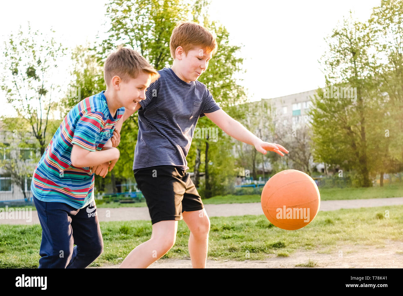 Due giovani ragazzi a caccia di un pallone da basket mentre si pratica il loro gioco all'aperto su un campo da gioco nel caldo bagliore del sole Foto Stock