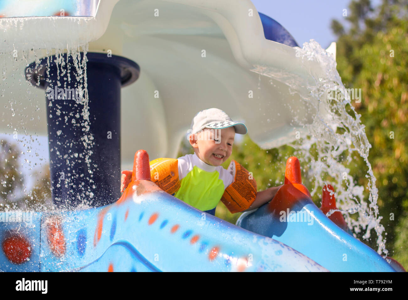 Un piccolo ragazzo rotola giù uno scivolo d'acqua. La gioia dei bambini nel parco acquatico. Vacanze estive per ragazzi nel parco acquatico. Turchia Antalya. Foto Stock
