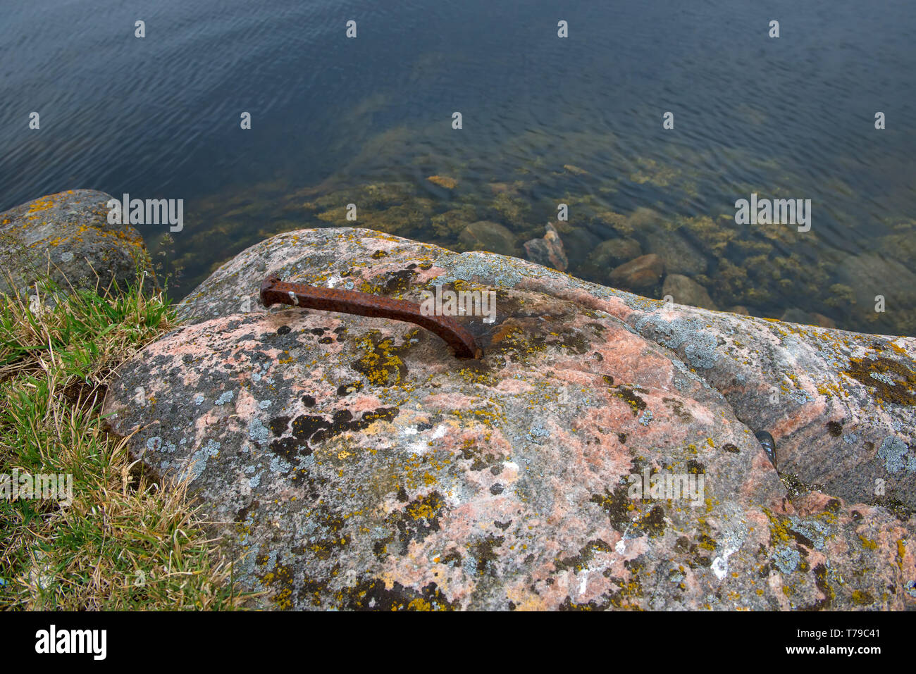 Un vecchio arrugginito staffa è trascinato in un grande masso per trattenere parti di una vecchia diga. Foto Stock