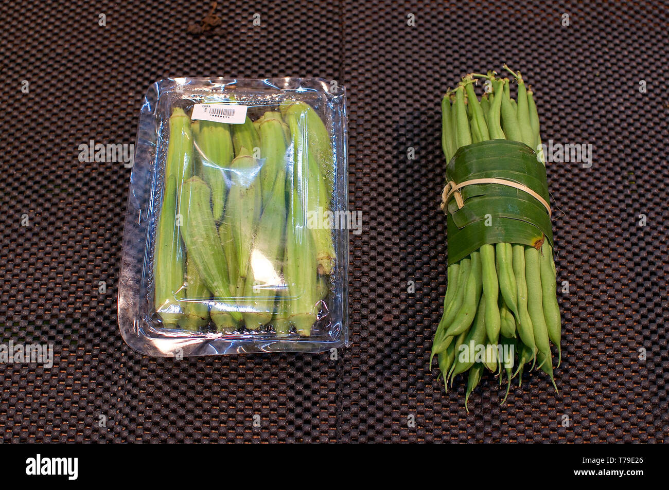 L'Okra raggruppati in una confezione di plastica e fagioli avvolti in foglie di banana tenuto in mani femminili. Questa è una soluzione eccellente come sostituire la confezione di plastica una Foto Stock
