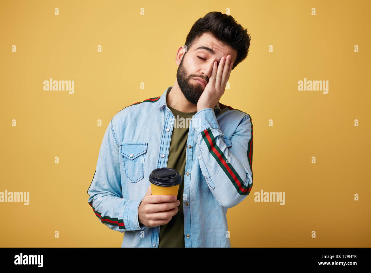 Stanco esaurito studente con espressione assonnato, copre il viso con palm, trattiene la carta monouso tazza di caffè. l uomo non vuole andare a lavorare isolati Foto Stock