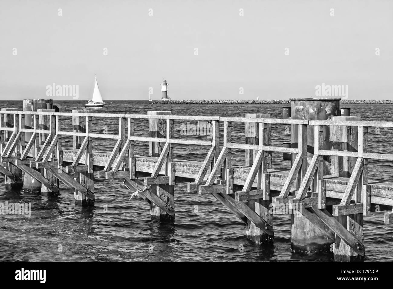 Immagine monocromatica del Mar Baltico con il molo in legno, faro e nave a vela a Rostock Warnemuende, Germania Foto Stock