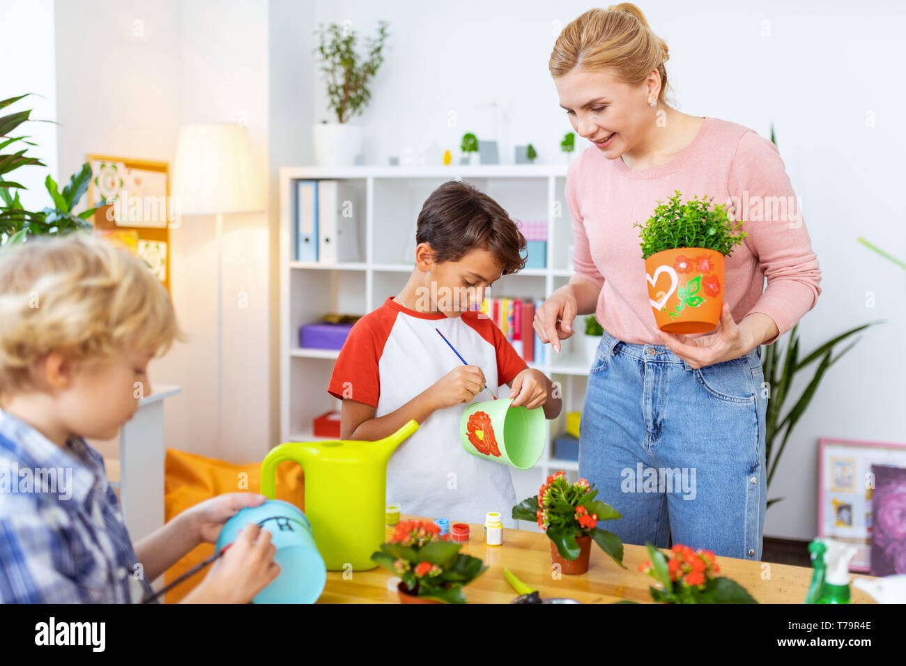 Tempo verniciatura. Biondo e trasmissione via IR di ecologia insegnante osservando il suo grazioso alunni i vasi da fiori di colorazione Foto Stock