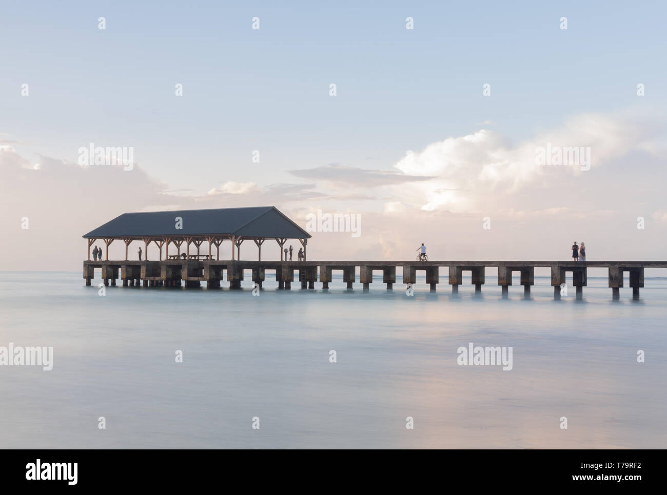 Acqua calma circonda il molo al tramonto sul molo di Hanalei in Kauai Hawaii con una lunga esposizione per smussare le onde per creare la scena pacifica Foto Stock