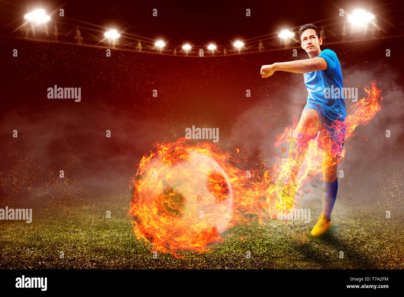 Asian giocatore di football uomo in maglia blu con calci la palla con effetto fuoco sul campo di calcio a Stadium Foto Stock