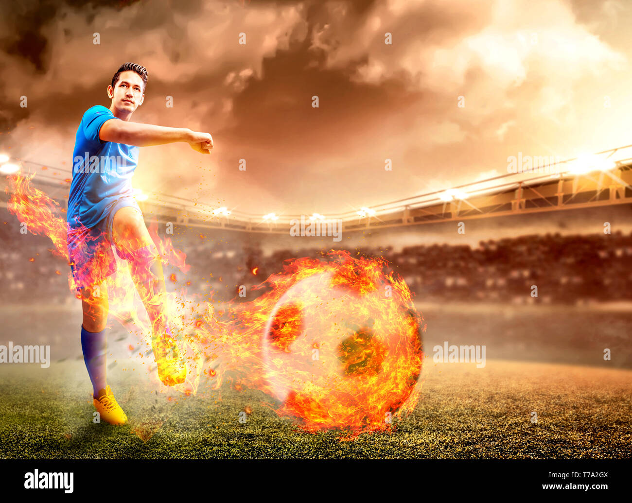 Asian giocatore di football uomo in maglia blu con calci la palla con effetto fuoco sul campo di calcio a Stadium Foto Stock