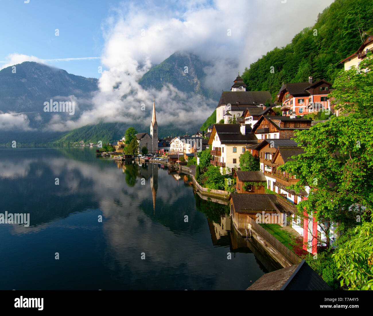 La mattina presto il colpo di Hallstatt village e riflessi nell'acqua ancora di Hallstatter vedere (lago Hallstatt) con basse nubi sulla collina Foto Stock