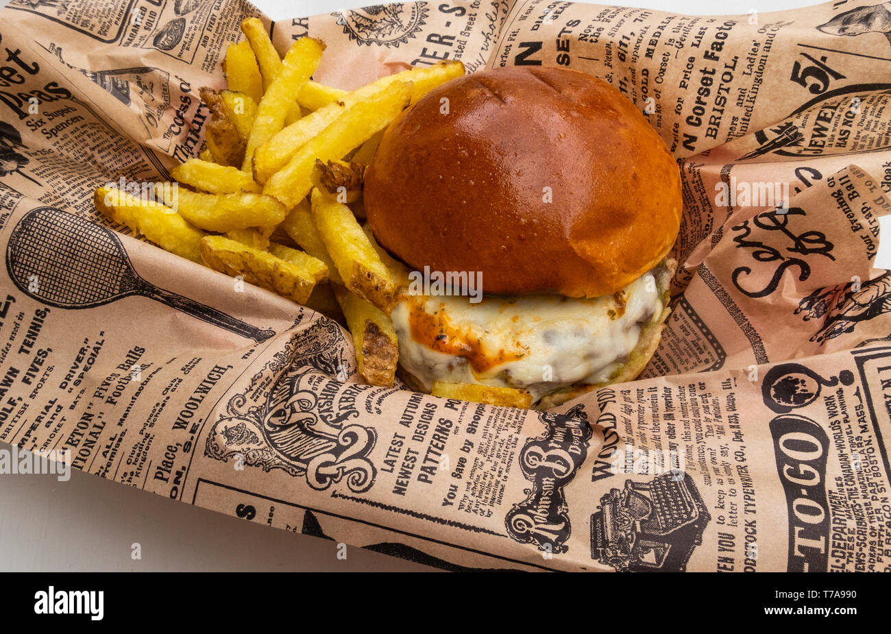 Un cheeseburger e patatine fritte con un tocco di piccante salsa calda avvolti in un giornale Foto Stock