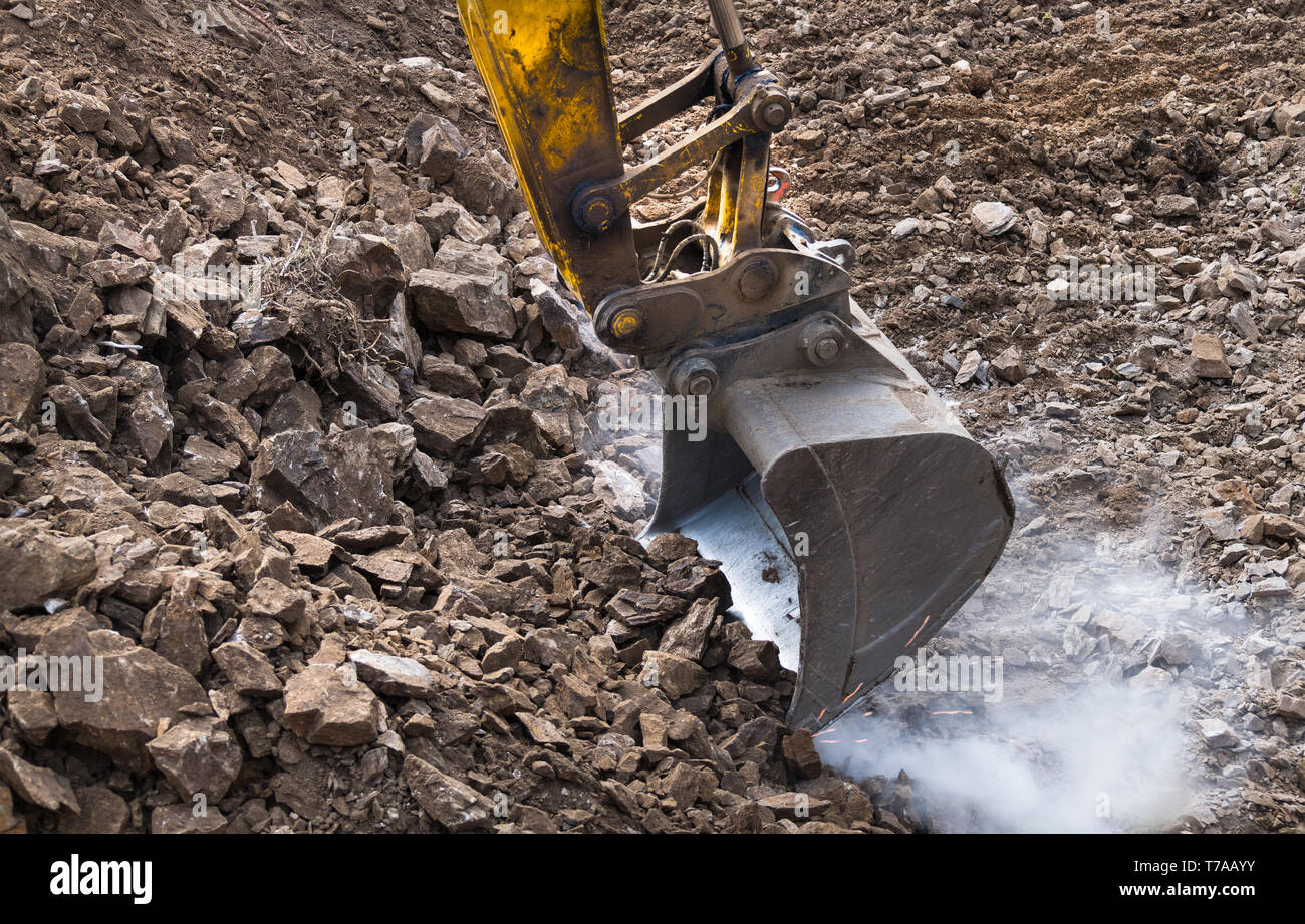 Lavoro benna di un escavatore. Scintille. Polveroso sito in costruzione. Macchina di scavo. Lavori di scavo. Pala di alimentazione in movimento terra e pietre. Scavatrice scoop. Foto Stock