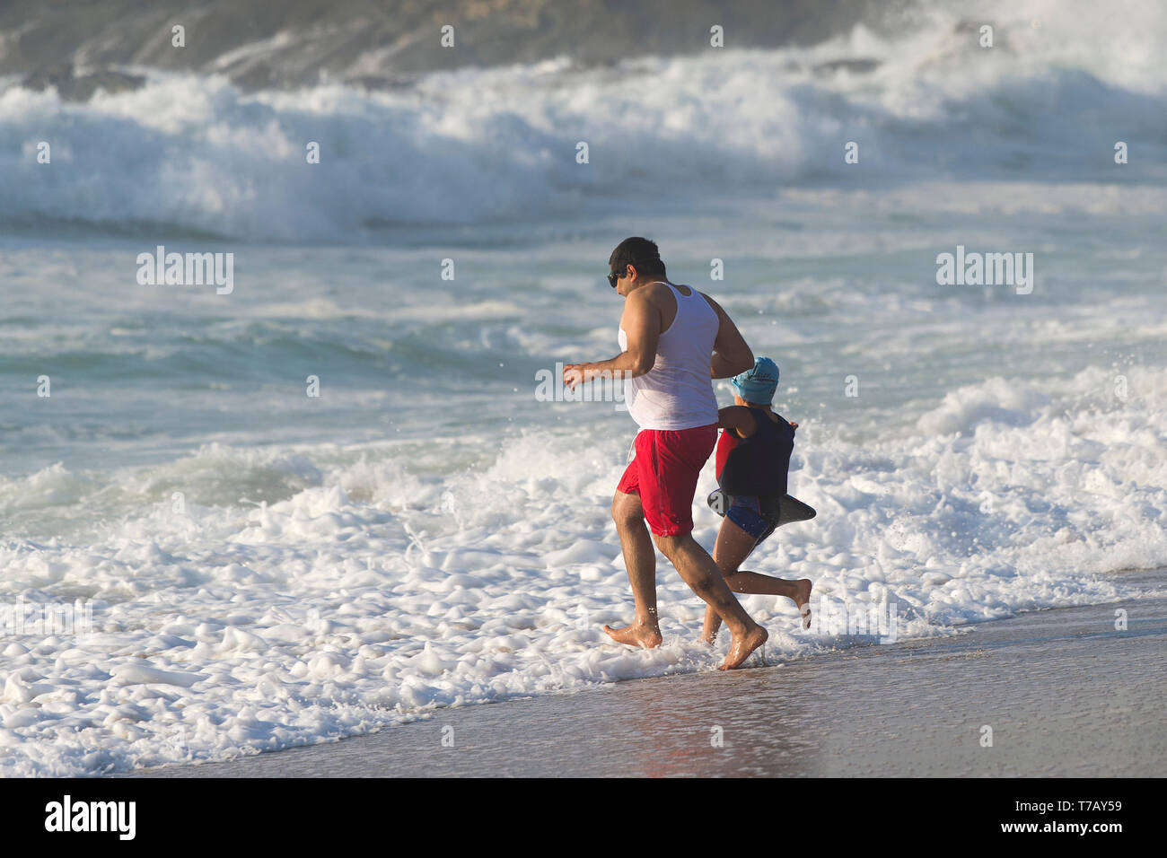 Un padre e la sua giovane figlia in una vacanza di staycation divertirsi correndo in mare a Fistral Beach a Newquay in Cornovaglia. Foto Stock