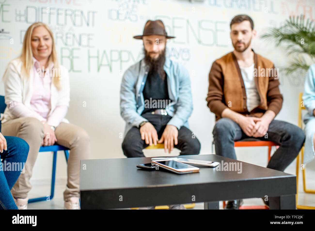 Gruppo di persone sedute insieme durante la terapia psicologica, avente dipendenza su gadget digitali in ufficio con telefoni sul tavolo Foto Stock