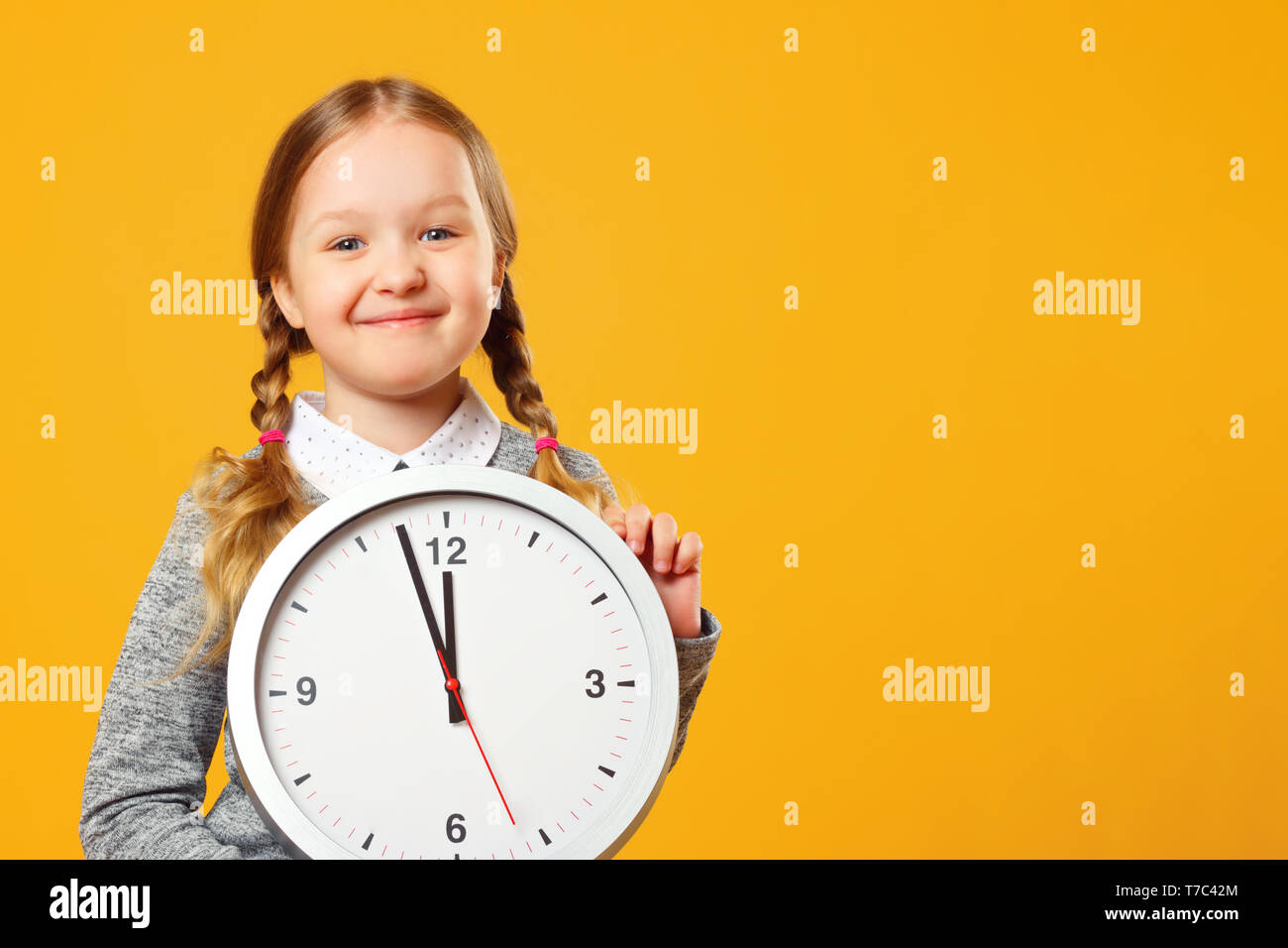Bambina tenendo un grande orologio su sfondo giallo. Il concetto di istruzione, scuola, scadenza, tempo per imparare. Foto Stock