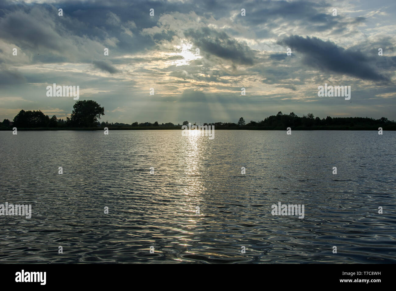 Il sole che tramonta dietro le nuvole di pioggia e riflettendo la luce nelle acque del lago - vista serale in Stankow, Lubelskie, Polonia Foto Stock
