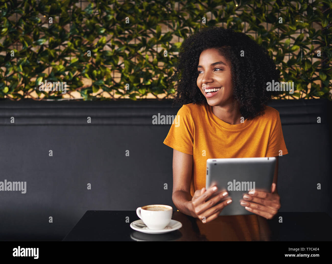 Felice giovane donna seduta al cafe azienda tavoletta digitale a portata di mano Foto Stock