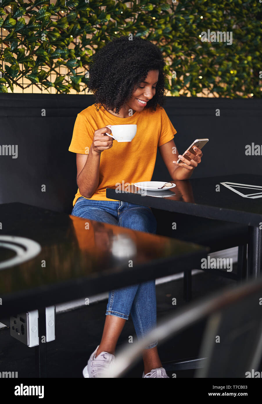 Donna che mantiene tazza di caffè utilizzando un cellulare in cafe Foto Stock