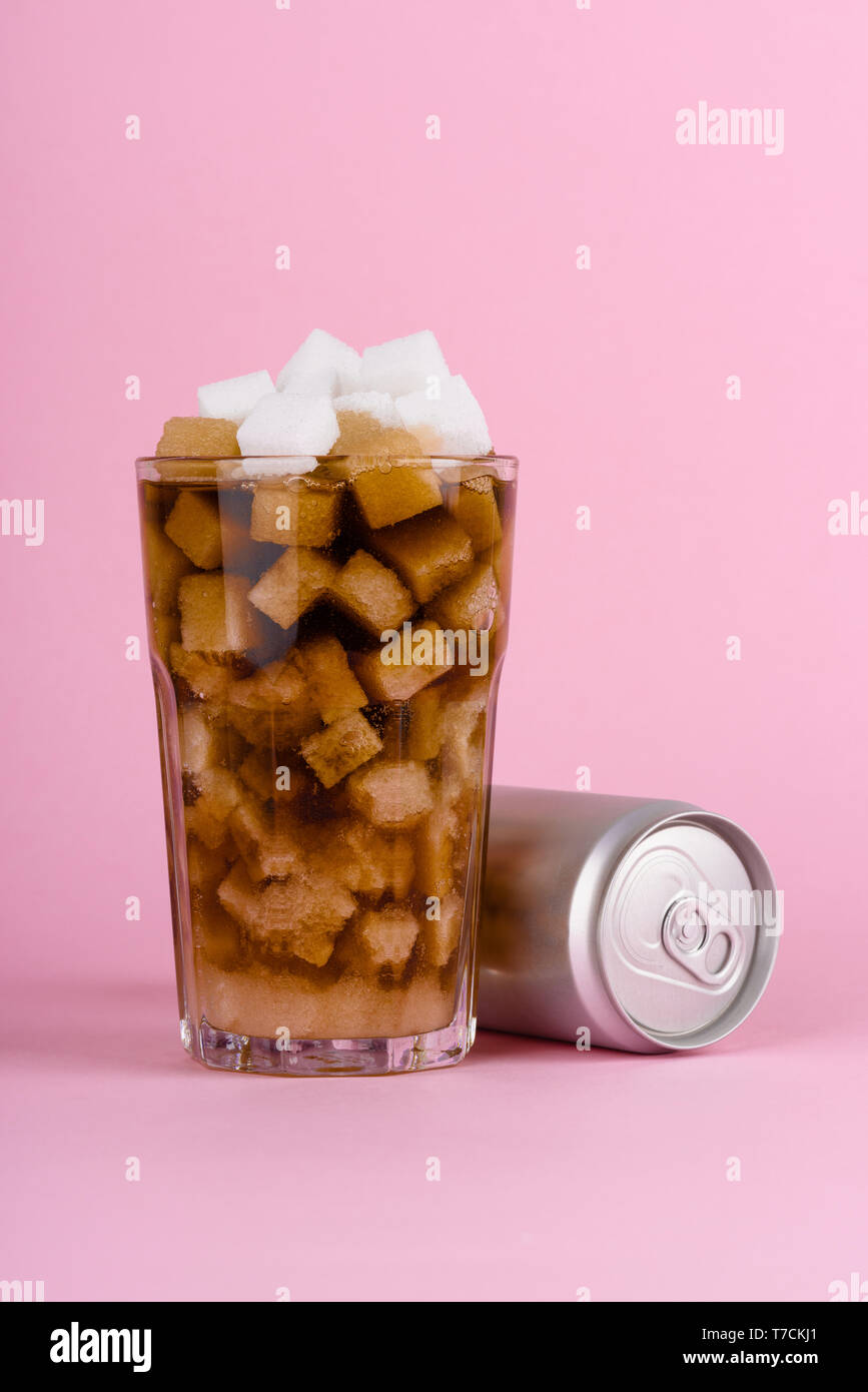 Bicchiere di grumo di cubetti di zucchero e soft drink cola con alluminio può rosa su sfondo color pastello. Dieta Unhealthly con dolce zuccherino di bevande analcoliche concetto. Foto Stock