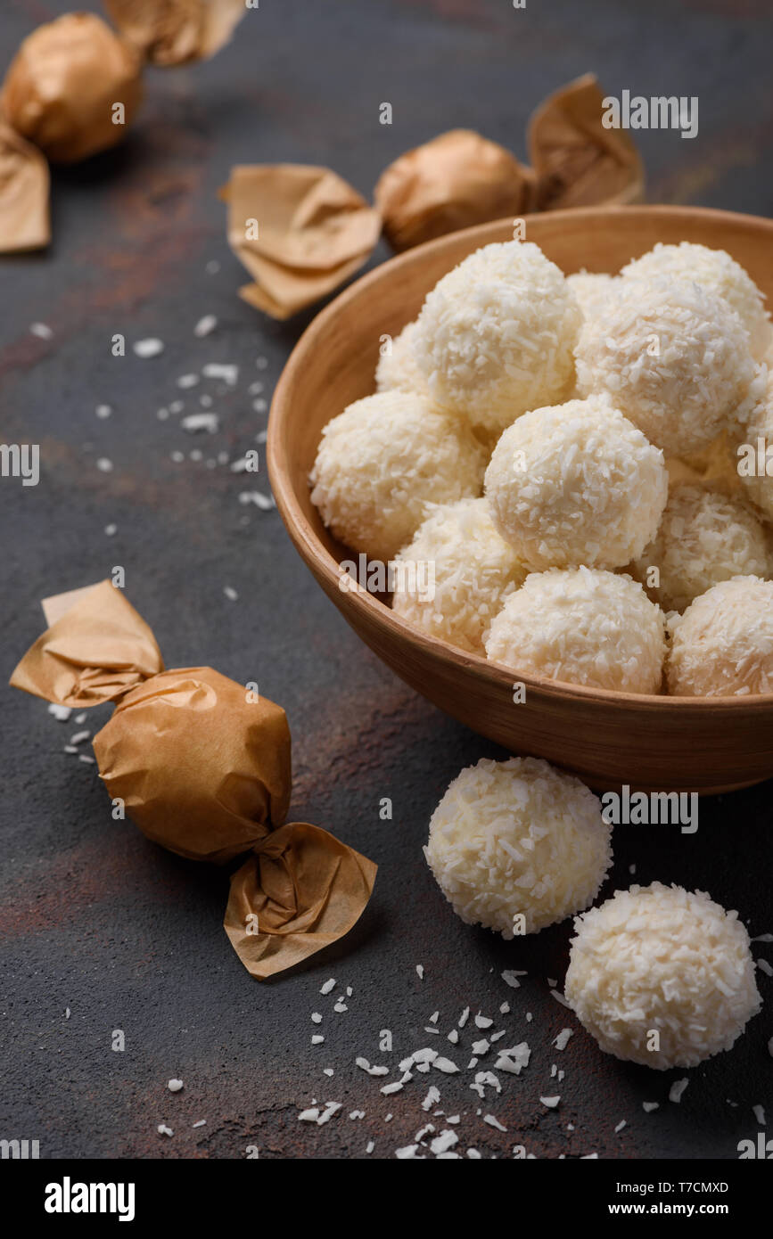 Di dolci al cocco nella ciotola e avvolto in carta su scuro dello sfondo della tabella Foto Stock