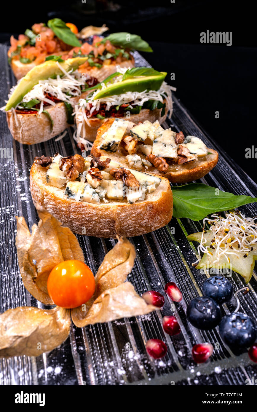 Antipasto bruschetta con formaggio, miele, noci e altri ingredienti su sfondo nero. Close-up. Il cibo italiano. Foto Stock