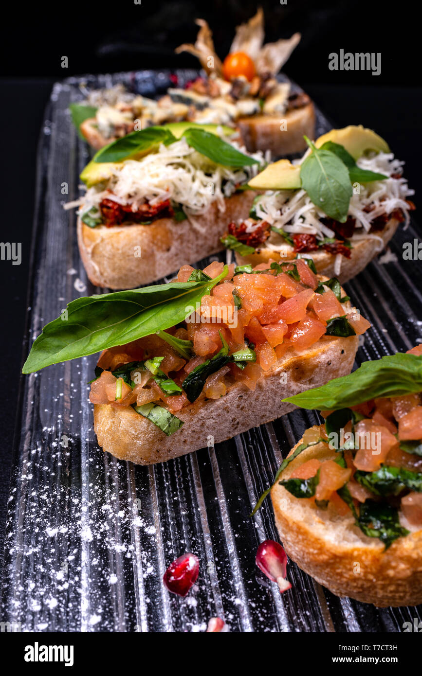 Stuzzicanti pomodoro antipasti italiani o bruschetta, su fette di pane abbrustolito baguette guarnita con foglie di basilico e avocado. Foto Stock
