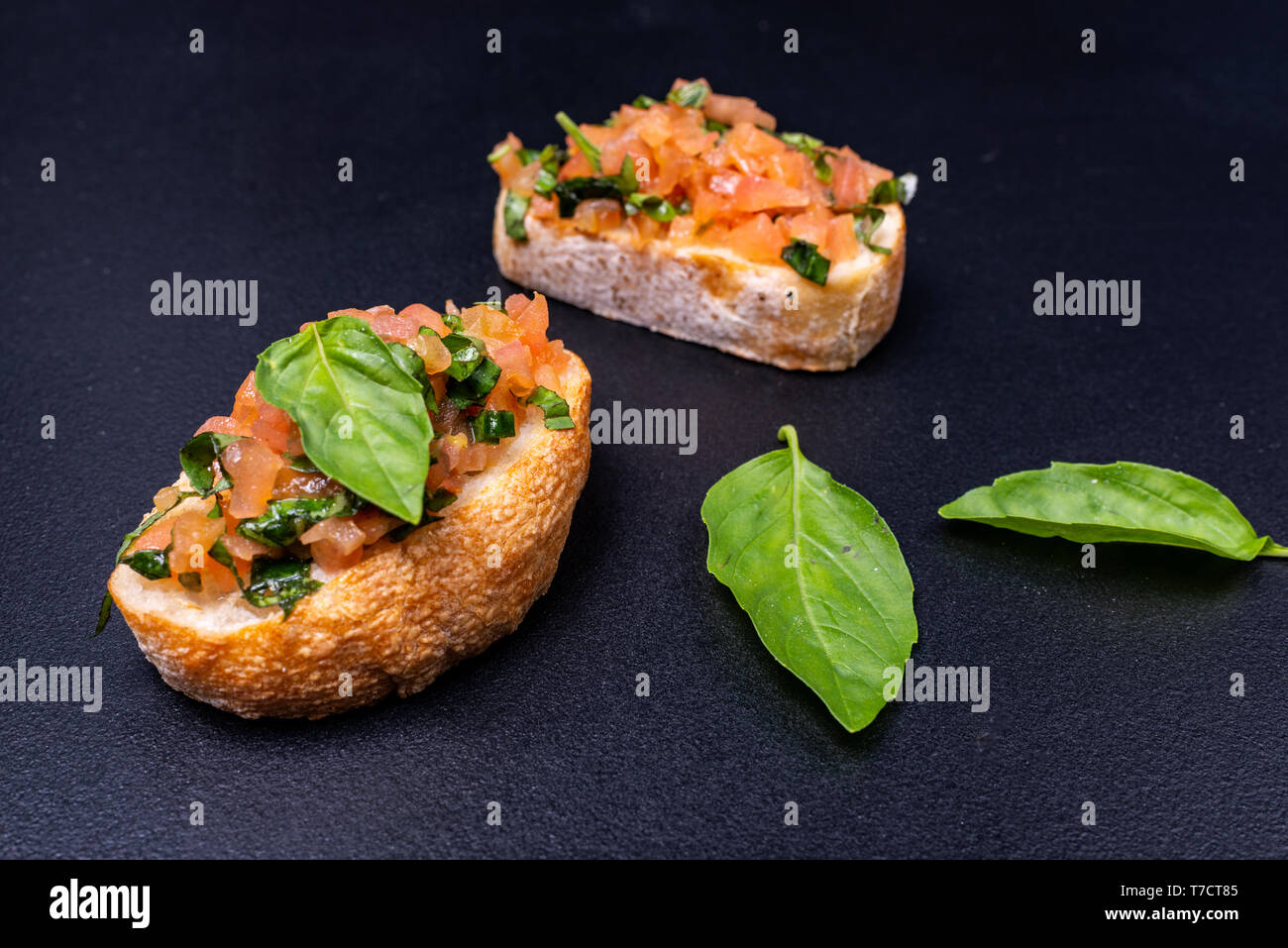 Stuzzicanti pomodoro antipasti italiani o bruschetta, su fette di pane abbrustolito baguette guarnita con basilico e avocado Foto Stock