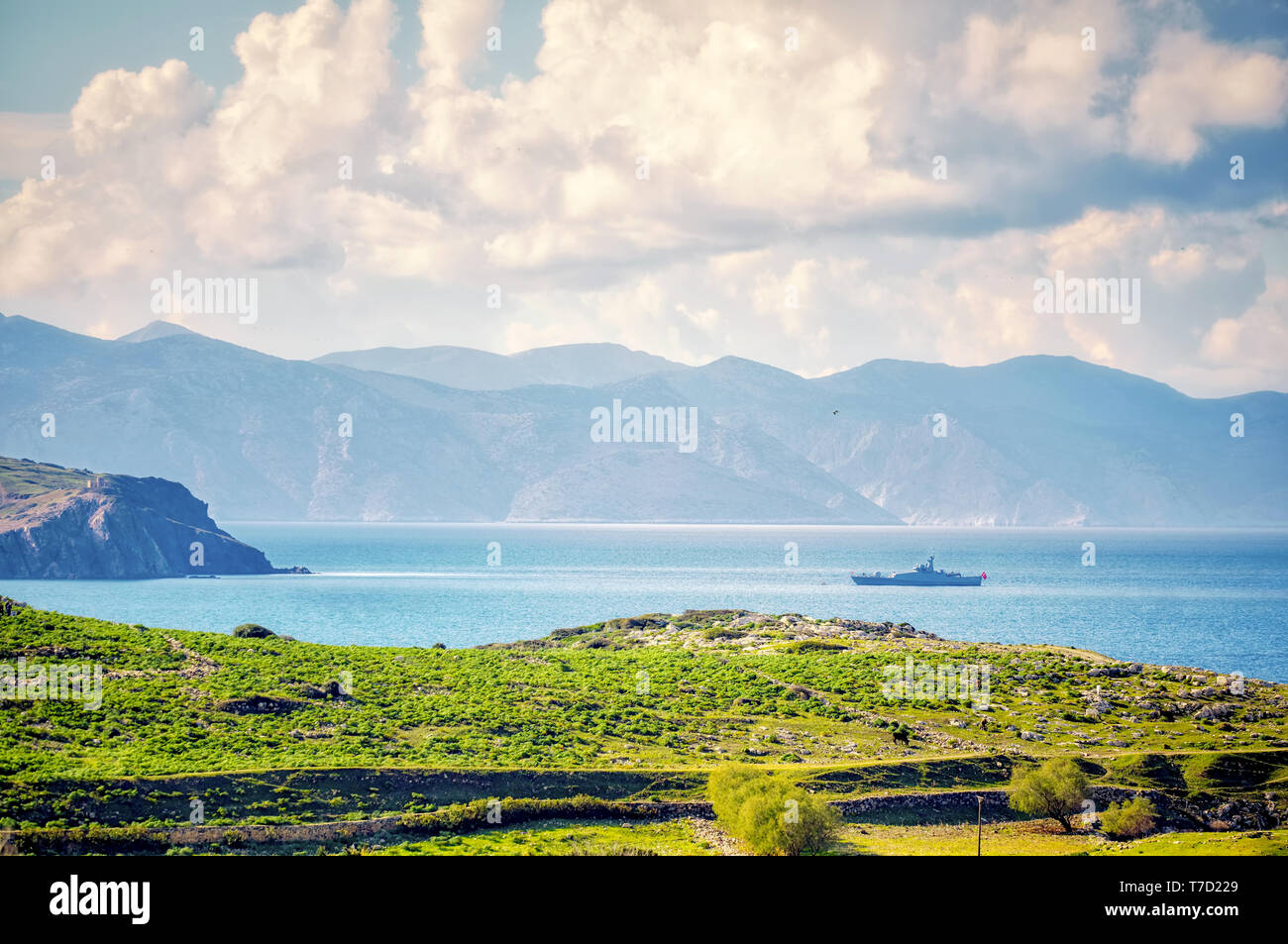 Dalla vista al di sopra di un campo di prato, mare, cielo, nuvole, montagne e una guardia costiera della barca di assalto in Gumusluk, Bodrum, Mugla, Turchia Foto Stock